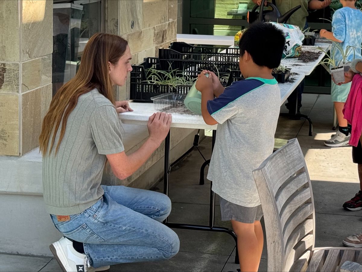 Student plants gardening seeds with younger students